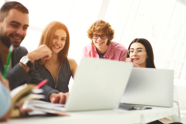 istock Group of  smiling talented students celebrating winning university contest for developing best  software working together using modern laptop computers and wireless connection to internet in classroom 905464044