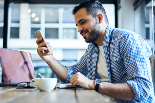 istock Cheerful bearded male developer waiting for meeting with partners dealing with outsourcing drinking coffee and chatting via modern smartphone using wireless connection to free 4G internet in cafe 905464524