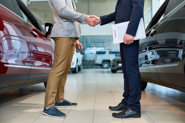 People Shaking Hands in Car Showroom Low section side view of  handsome client shaking hands with sales manager in car showroom, after buying brand new luxury car car show photos stock pictures, royalty-free photos & images