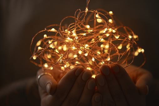 hands of a girl holding a garland of Christmas lights on a dark background