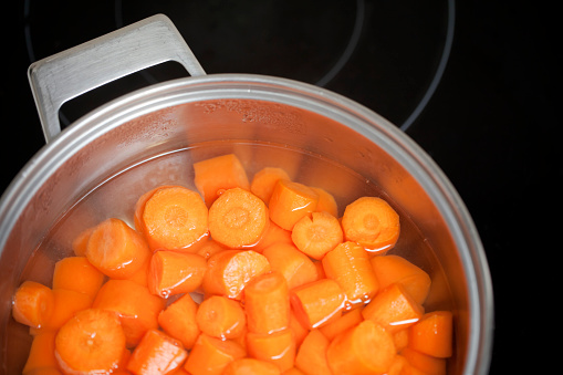 Carrots boiling in the pot with handle on a glass-ceramic stove top. copy space available.