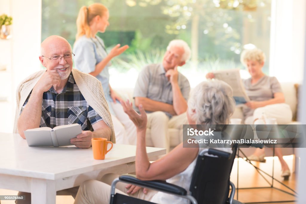 Man talking with disabled woman Elderly man talking with disabled woman while sitting together at table in common room Senior Adult Stock Photo