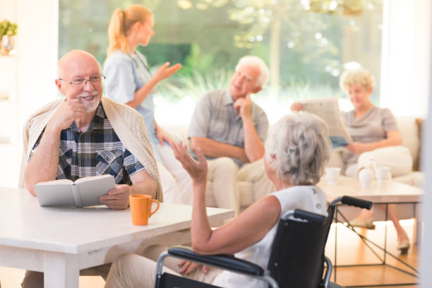 Man talking with disabled woman Elderly man talking with disabled woman while sitting together at table in common room assisted living stock pictures, royalty-free photos & images