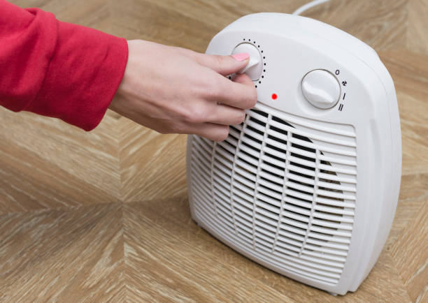 Woman warms her frozen hands near an electric fan heater at home. Selective focus. Woman warms her frozen hands near an electric fan heater at home. Selective focus. warms stock pictures, royalty-free photos & images