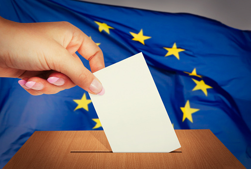 Hand putting a voting ballot into the box and flag of European Union on the background