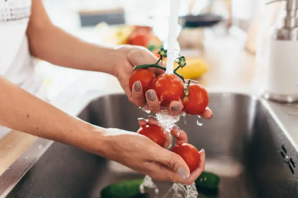 Photo of Woman washing tomatoes in kitchen sink close up.
