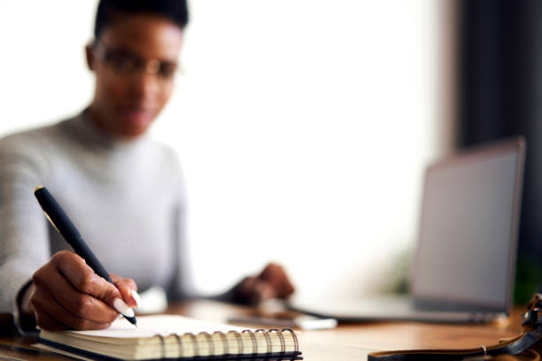 Talented female writer work on creation new novel while noting ideas in personal diary to choose best plot strategy to attract readers concentrated on work in personal cabinet, selective focus on pen