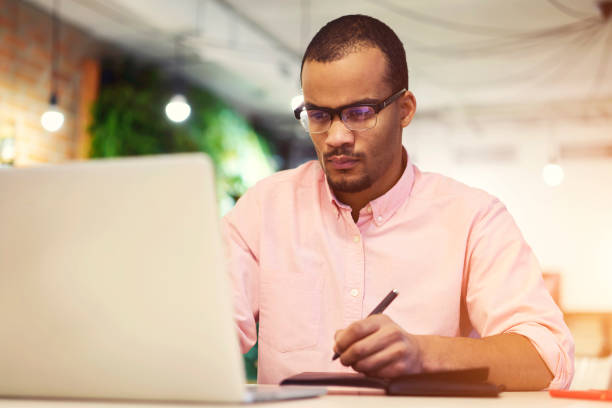istock Confident male project manager responsible for the strategy and implementation of individual projects checking work of freelancers finishing creation of startup project noting best ideas into notebook 905489680