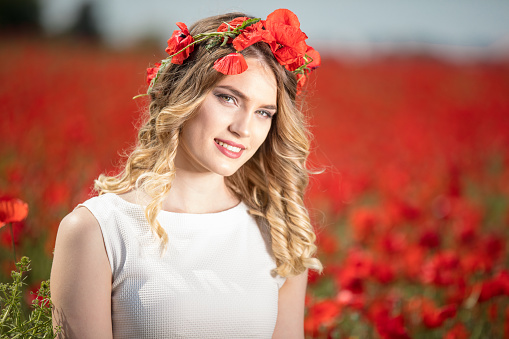 portrait of elegant young woman with long hair and straw hat in poppy field in evening sunlight