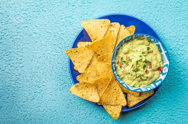 Mexican nachos with guacamole Mexican nachos, tortilla chips with guacamole sauce over blue background, top view guacamole stock pictures, royalty-free photos & images