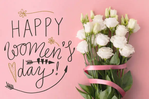 From above Happy Women's day words and bunch of flowers with ribbon on pink background.