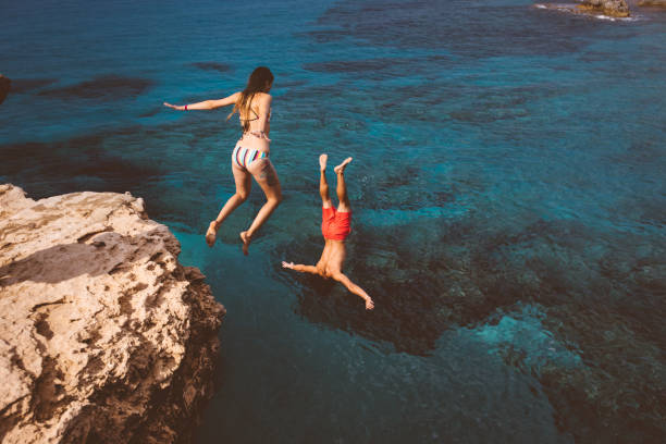 Active couple diving from high cliff into ocean Young couple jumping off high cliff rock into the sea on tropical island summer vacations cliff jumping stock pictures, royalty-free photos & images