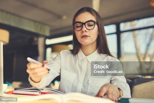Portrait Of Concentrated Skilled Female Literary Editor Working With Articles For Magazine Correcting Mistakes And Editing Composition While Sitting At Desk In Modern Coworking Space With Stationery Stock Photo - Download Image Now