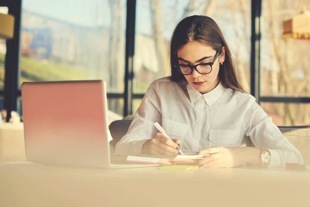 istock Creative female copywriter making text for advertising campaign and scripts for radio jingles and TV commercials noting best ideas to copybook before sending to ceo via email using laptop computer 905497556