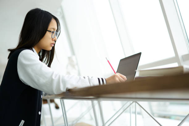 istock Young female pupil preparing homework task doing training exercises from online manual book on school webpage using laptop computer and wireless connection to internet while sitting in classroom 905497704
