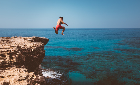 Brave man diving from high cliff into blue sea waters on tropical island summer adventure