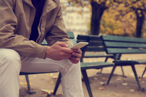 istock Attractive man texting on his smart phone while sitting on the bench in park. 905503832