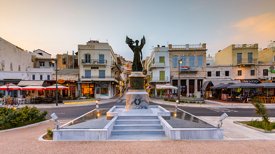 Ermoupoli, Greece - May 13, 2017: Statue and coffee shops at the seafront of Ermoupoli town on Syros island in Greece.