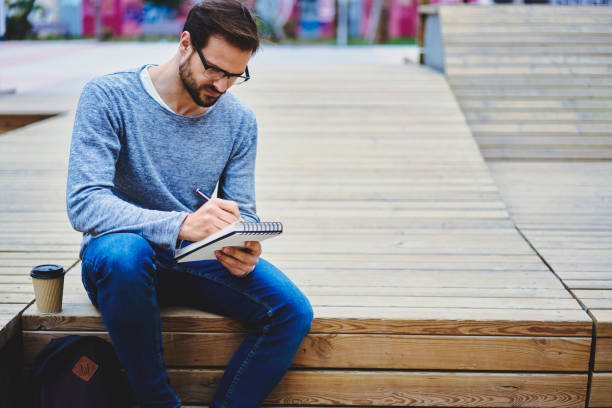 istock Handsome young male international student preparing homework task creative concept for own business startup project sitting outdoors in campus area with backpack and notepad to write down ideas 905504464