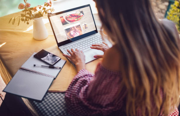 Female food blogger using laptop and working from home Young food blogger entrepreneur writing blog post and working online on laptop from home office looking over shoulder stock pictures, royalty-free photos & images