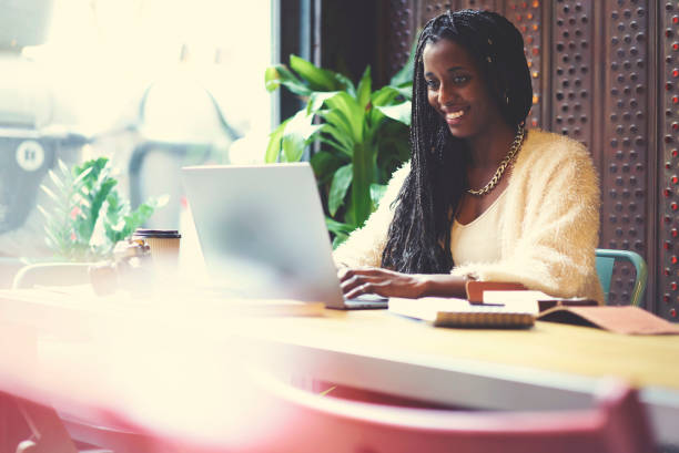 copywriter américain afro souriant satisfaits de tâche de travail accomplie téléchargement de fichiers multimédias à l’aide de l’ordinateur portable, journaliste créative faisant tâche distante dans café intérieur frappe message dans le chat - lundi noir chinois photos et images de collection