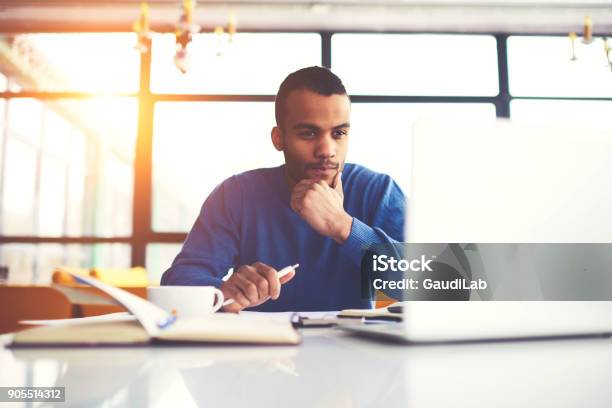 Pensive International Afro American Student Watching Training Webinar On Laptop Computer Improving Skills And Knowledge Concentrated Dark Skinned Freelancer Pondering On Completing Working Tasks Stock Photo - Download Image Now