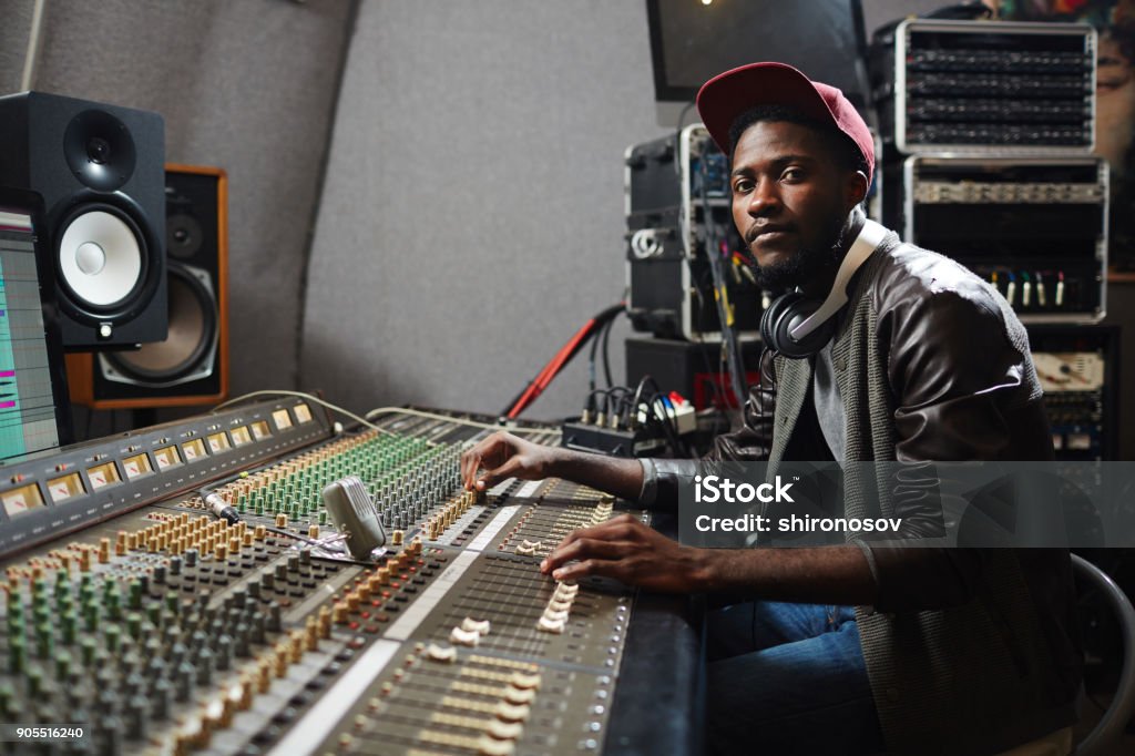 Recording rap Modern young singer in rapper attire working in audio studio by recording equipment Producer Stock Photo