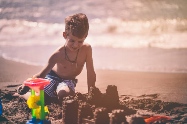 istock Little boy on summer holidays building sandcastles on beach 905520660