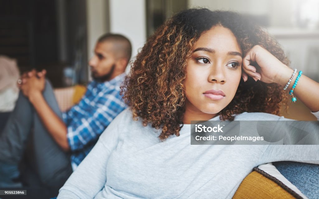 Who's going to break the tension? Shot of a young woman looking upset after a fight with her husband in the background Couple - Relationship Stock Photo