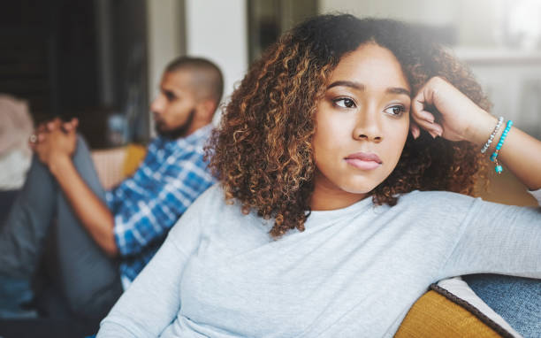Who's going to break the tension? Shot of a young woman looking upset after a fight with her husband in the background gloomy mood stock pictures, royalty-free photos & images