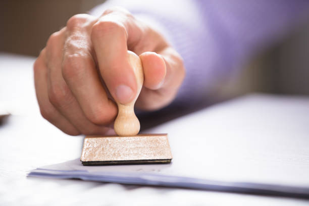 Close-up Of A Person Stamping On Document Close-up Of A Person's Hand Stamping On Approved Application Form Over The Desk beatification stock pictures, royalty-free photos & images