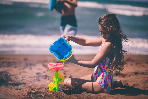 Little girl on island summer family vacations playing with toys on beach sand