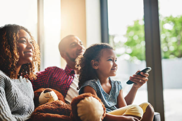 Weekends are about doing what everybody loves Shot of a happy young family of three watching tv from the sofa at home lens flare offspring daughter human age stock pictures, royalty-free photos & images