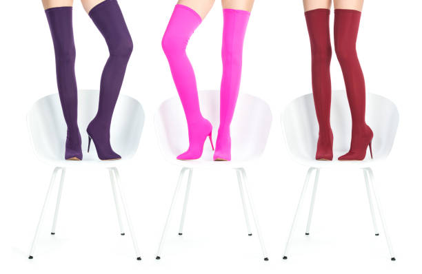 Side view of anonymous female with shadow of raised legs in yellow colored long socks and pink fuchsia shoes while sitting on violet background