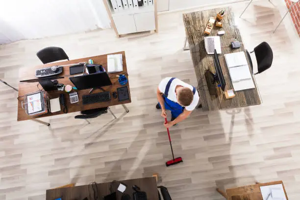 Elevated View Of Male Janitor Cleaning Floor With Broom At Workplace