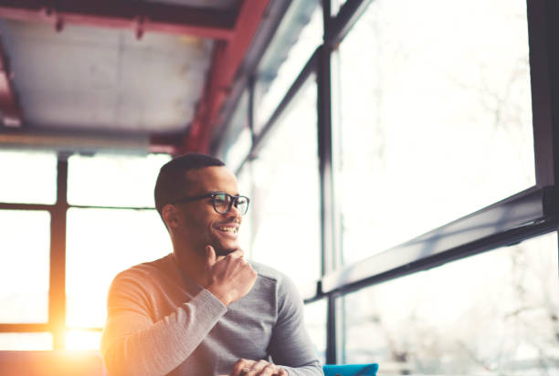 mec gai hipster américain afro tendance spectacles assis dans loft café intérieur au repos dans la bonne humeur, souriant jeune homme peau sombre satisfait des projets achevés avec succès - lundi noir chinois photos et images de collection