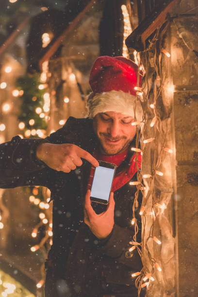 istock Man with blank screen smart phone and Christmas lights decoration. Technology and holidays concept. 905549210