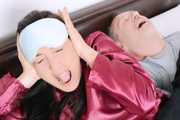 Portrait of irritated woman blocking ears with hands while man snoring on bed Portrait of irritated woman blocking ears with hands while man snoring on bed. Indoors sleep with deam hero mouth guard stock pictures, royalty-free photos & images