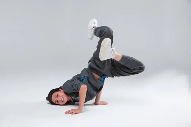 Photo of An active little boy dancing lying on chest resting arms, bending legs in lap. On a gray background.