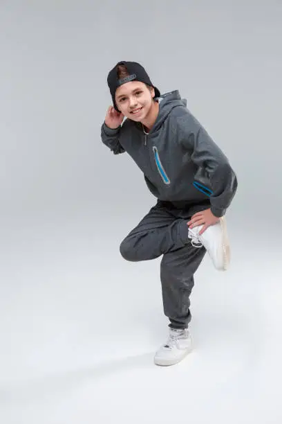 Photo of A happy little boy stands on one leg with his other leg. On a gray background.