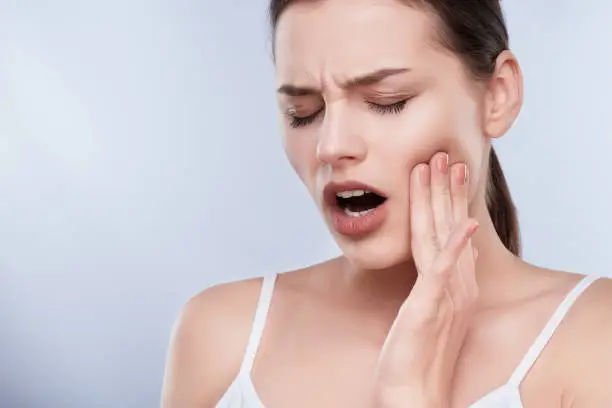 Toothache, white teeth. Head and shoulders of young woman suffering from toothache, teethcare. Painful expression on face of woman, hands near face, closed eyes