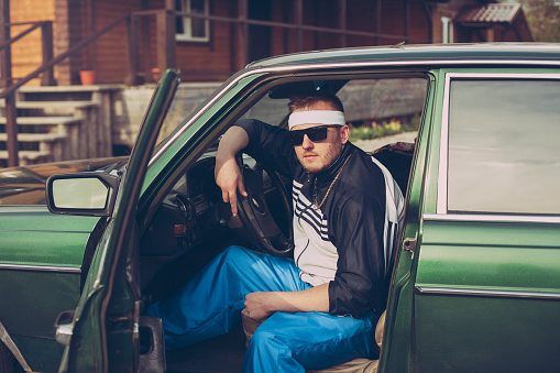 guy in the nineties sits behind the wheel of a car wearing sunglasses