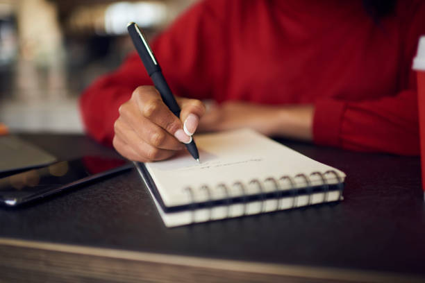 istock Selective focus on handwriting in spiral notebook creating to do list with targets on white page, cropped image of afro american female designer drawing sketches for project in diary with pen 905583536