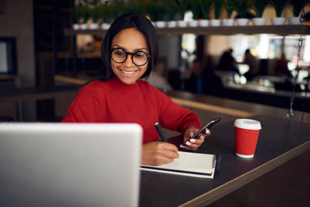 joyeux afro américain étudiant en lunettes regarder la vidéo sur ordinateur portable tout en faisant les devoirs dans le café, qualifiés marketing expert lecture nouvelles de page web sur l’ordinateur portable création de stratégie dans le bloc-notes de charme - lundi noir chinois photos et images de collection