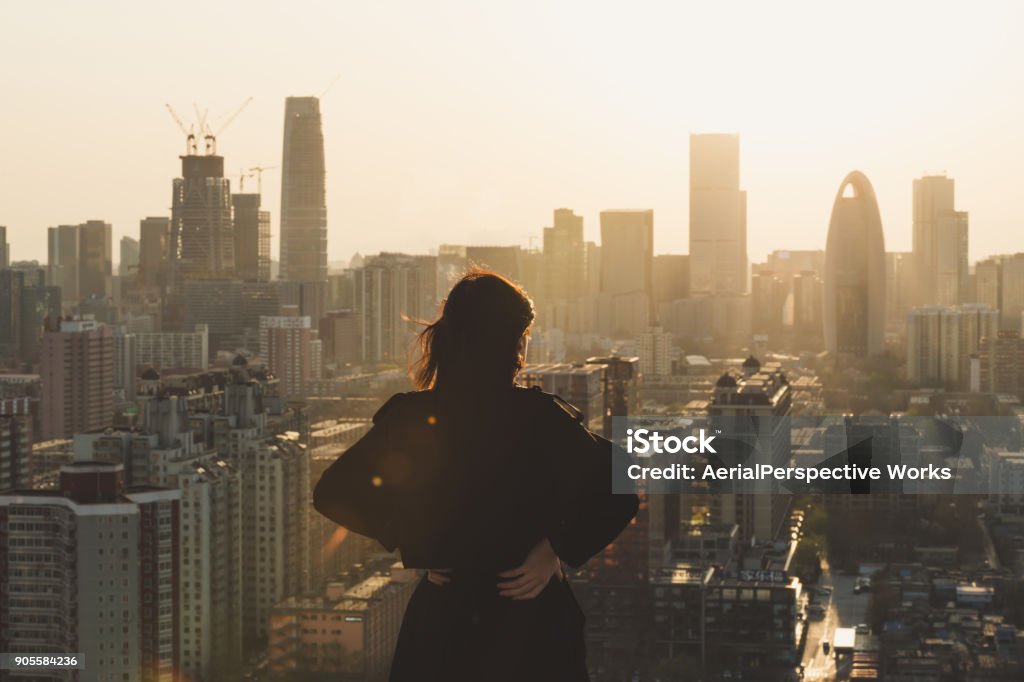 Rear view of Woman looking at city in Sunlight City Stock Photo