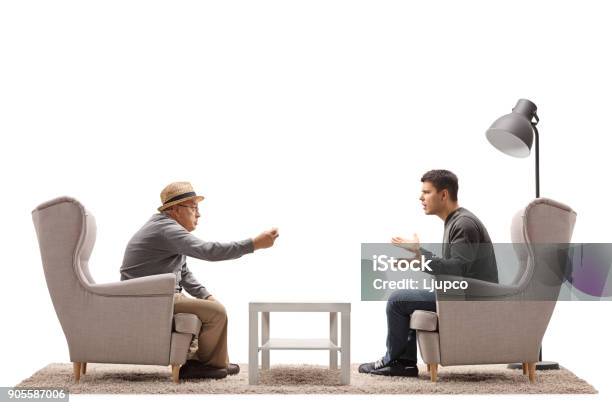 Mature Man And A Young Guy Seated In Armchairs Arguing Stock Photo - Download Image Now