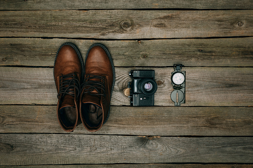 Flat lay of brown shoes with film camera and compass on a wooden table