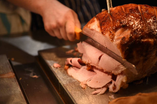 food photography image of a traditional roast joint of gammon or ham with a hand and carving knife slicing the juicy hot meat ready to serve and on a dark blur background - nobody uk indoors british culture imagens e fotografias de stock