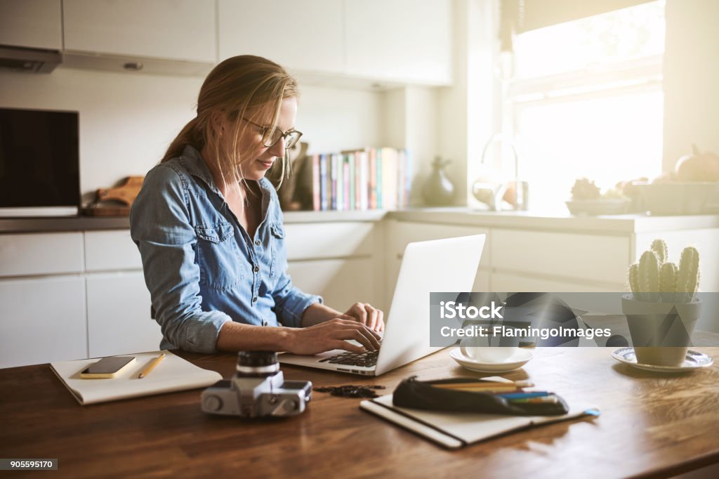 Junge Frau sitzt in ihrer Küche auf einem Laptop arbeiten - Lizenzfrei Arbeiten von Zuhause Stock-Foto