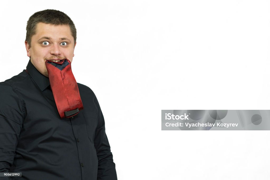 Young man posing. In the teeth holds a mobile phone. The manager is eating a tie. Young man posing. In the teeth is a mobile phone. White background. The manager is eating a tie. 20-29 Years Stock Photo